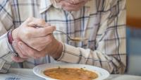 older man struggling to eat soup due to an essential tremor