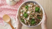Japanese-style rice bowl with flaked fish, green vegetables, and soy seasoning on a wooden table