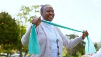 A woman exercises outdoors using a resistance band.