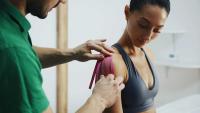 A clinician applies kinesiology tape to a woman’s shoulder.