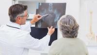 A clinician shows a patient a hip X-ray and points to the joint.