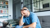 older man holding his face in his living room