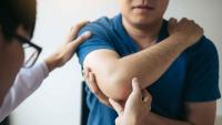 A clinician palpating the inner elbow while evaluating elbow pain in an adult patient.