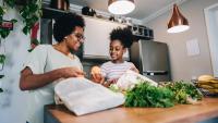 Mother and daughter talking and unpacking fruits and vegetables in the kitchen at apartment