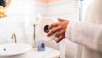 Hands holding a new roll of toilet paper in a bright, clean bathroom