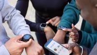 A group of four people standing in a circle, each holding a smartwatch in their hands.