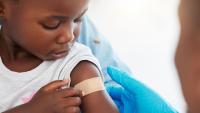 Child looking at a bandage on their upper arm after receiving a vaccination.