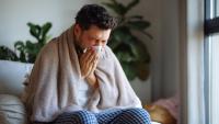 main with a blanket over shoulders blowing his nose