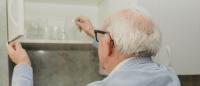 Older adult reaching into a kitchen cabinet to grab a glass.