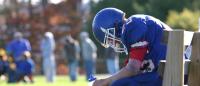 football player in pads and equipment on the bench with head hanging