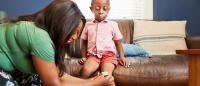 boy with scraped knee on couch and woman tending to wound