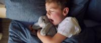 kid yawning in bed with stuffed bunny
