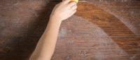 a hand cleaning dust off a wooden surface with a yellow sponge