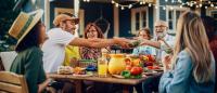 A family sits at a picnic table and shares a meal at a summer cookout.