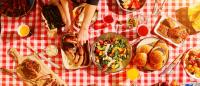 Food spread out on a picnic tablecloth during a summer cookout.