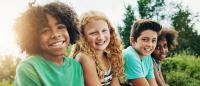Kids sit and smile during visit to woods while summer vacation.