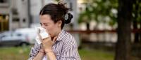 A young woman sneezing and reaching for tissues, signalling allergy issues.
