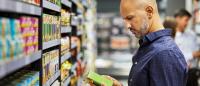 Man in blue shirt looks at box of food in grocery store.