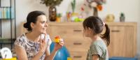 Female autism expert interacting with a young girl during a play-based session, using colorful wooden blocks in a cozy, child-friendly room