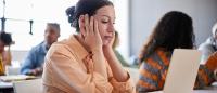 woman struggling to concentrate while sitting at a desk with her laptop in front of her