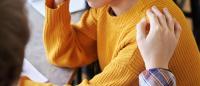 person with a hand on a a young persons should who is wearing a yellow sweater