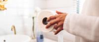 Hands holding a new roll of toilet paper in a bright, clean bathroom