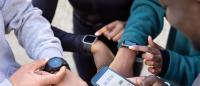A group of four people standing in a circle, each holding a smartwatch in their hands.