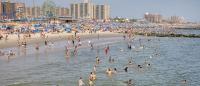 Crowded beach with people swimming and relaxing along the shore.
