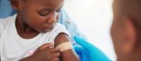 Child looking at a bandage on their upper arm after receiving a vaccination.